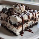 A decadent slice of no-bake ice cream cake layered with cream and chocolate cookies, drizzled with fudge.