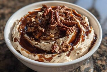A close-up of a creamy no-bake pecan pie dip topped with whole pecans and caramel sauce.