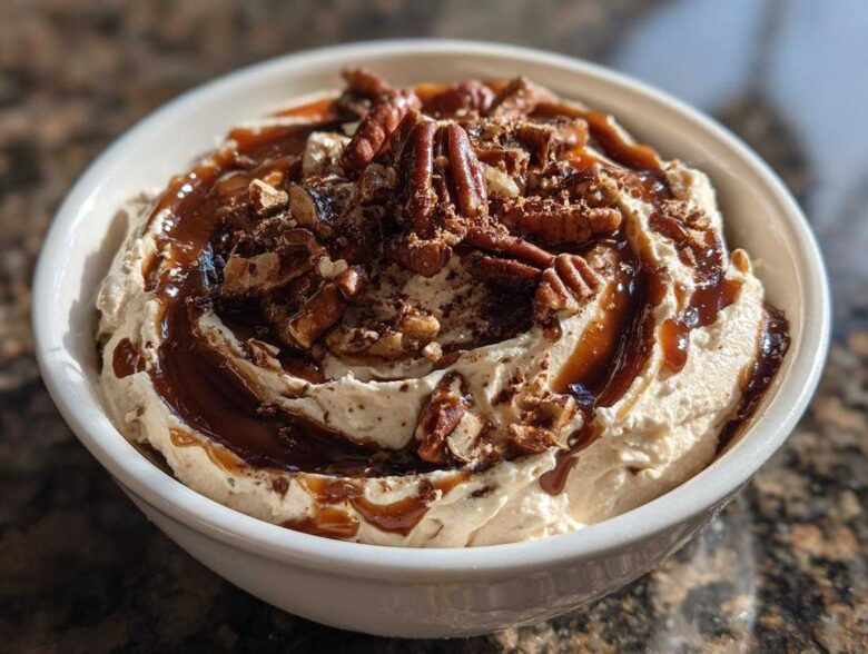 A close-up of a creamy no-bake pecan pie dip topped with whole pecans and caramel sauce.