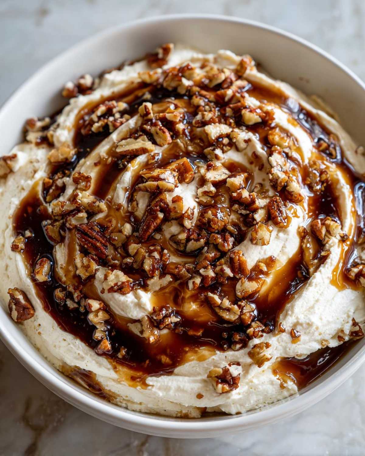A close-up of creamy no-bake pecan pie dip drizzled with caramel sauce and covered in chopped pecans.