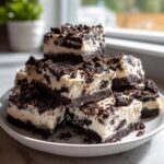 A stack of rich, creamy Oreo fudge squares featuring a dark chocolate base and white filling mixed with crushed cookies.