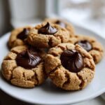 A close-up of several delicious peanut butter blossom cookies stacked on a white plate.