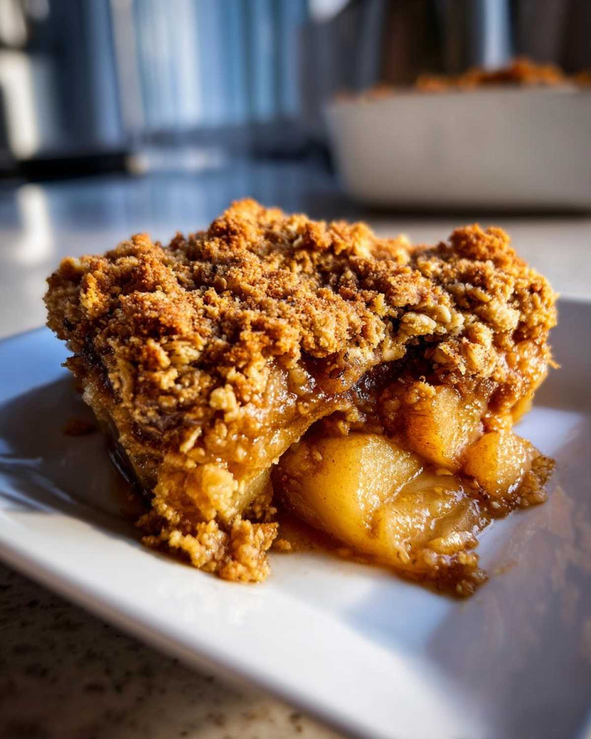A close-up shot of a square serving of warm pear crisp with a thick, crumbly topping and soft, syrupy pear filling.