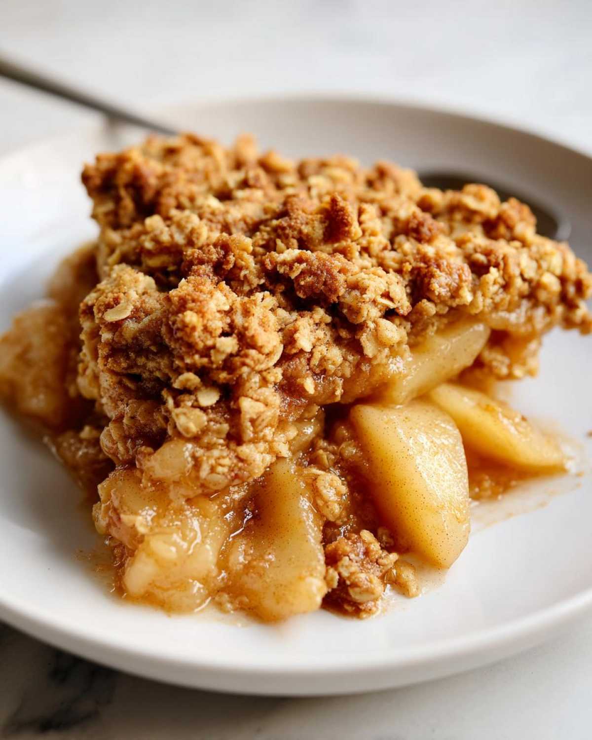 A close-up shot of a warm serving of pear crisp with a thick, crunchy oat topping over soft, spiced pears.