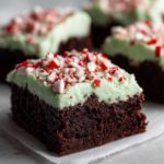 A close-up of a rich, dark chocolate peppermint brownie topped with light green mint frosting and crushed candy canes.