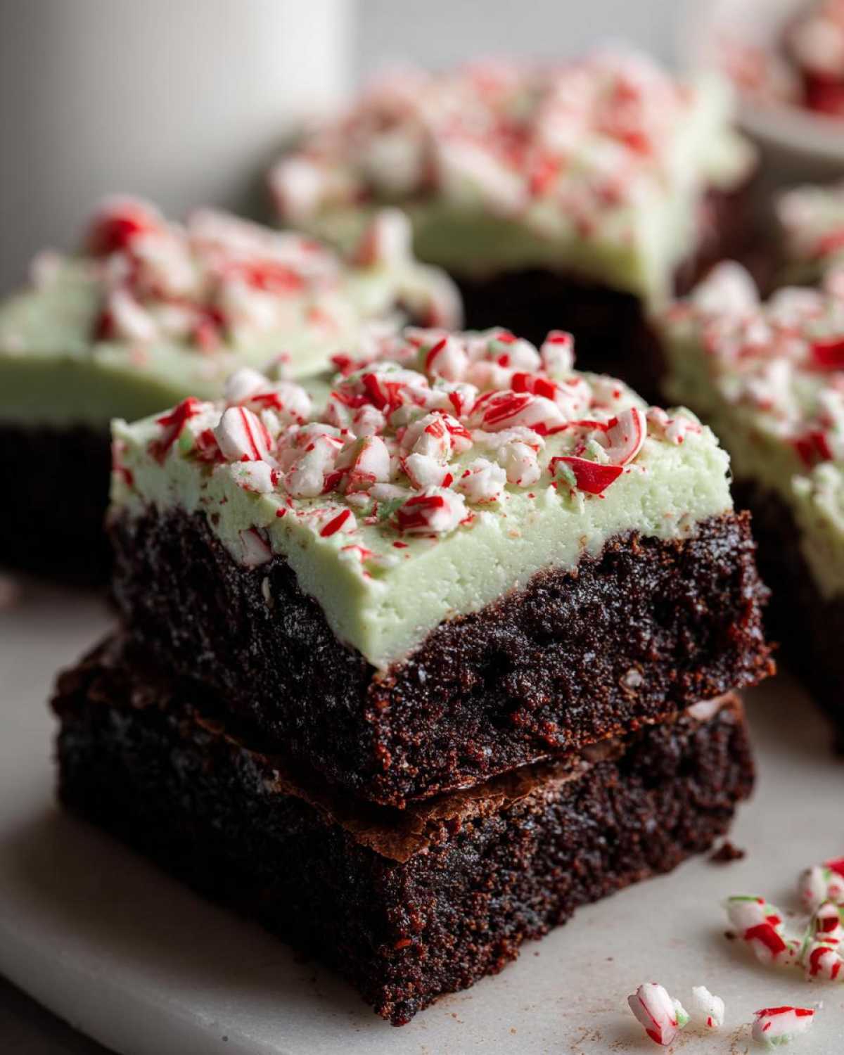 Close-up of two stacked, rich chocolate peppermint brownies topped with green mint frosting and crushed candy canes.