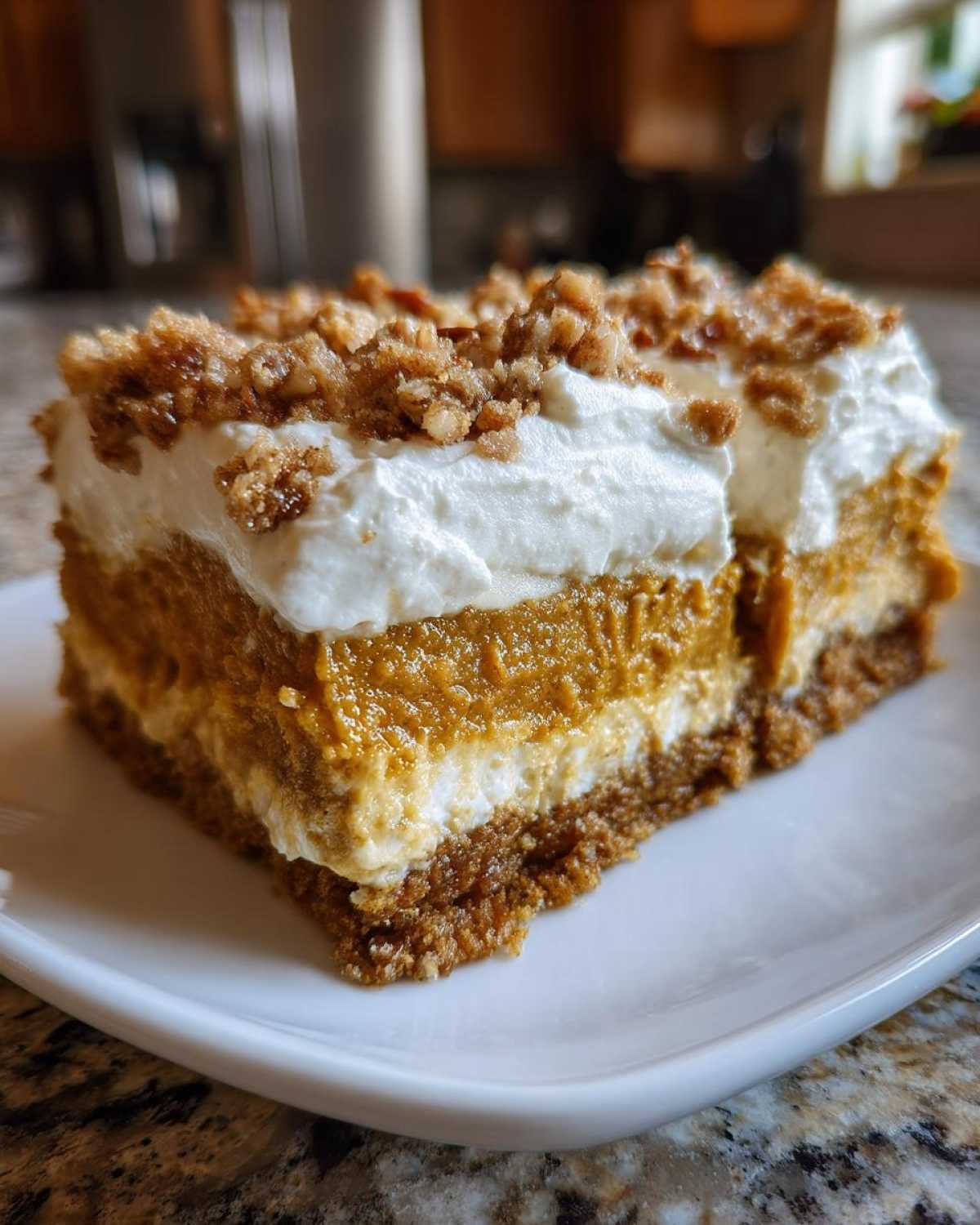 Close-up of a slice of three-layer pumpkin crunch dessert with whipped topping and streusel.