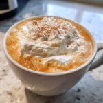 Close-up of a creamy pumpkin spice latte topped with a generous swirl of whipped cream and a dusting of cinnamon.
