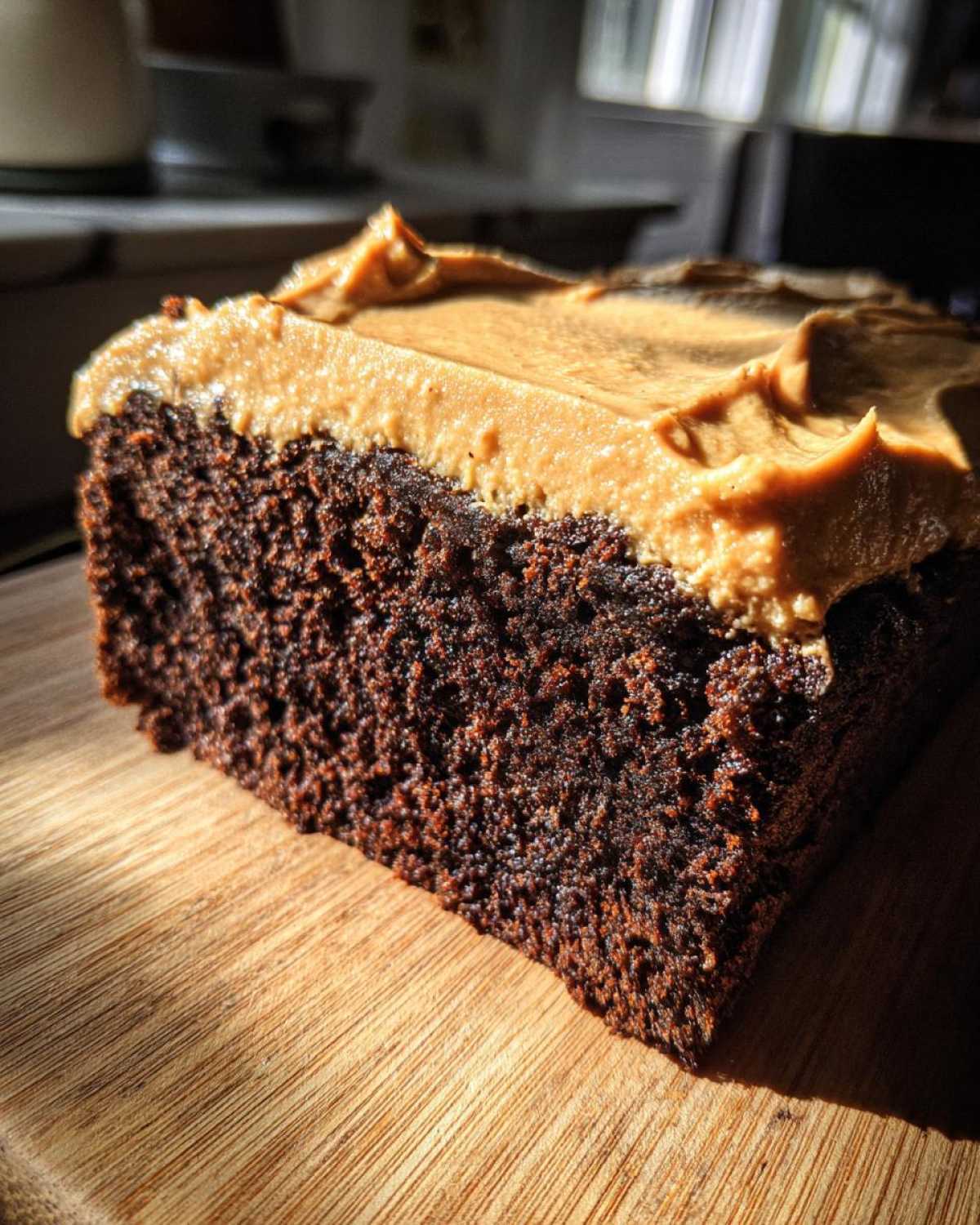 Close-up of a moist slice of dark gingerbread cake topped with thick, light brown frosting.