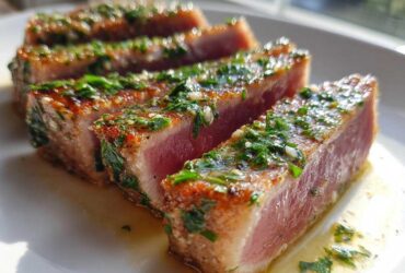 Close-up of four thick slices of seared tuna steak, showing a rare pink center and topped with a bright green herb and garlic marinade.