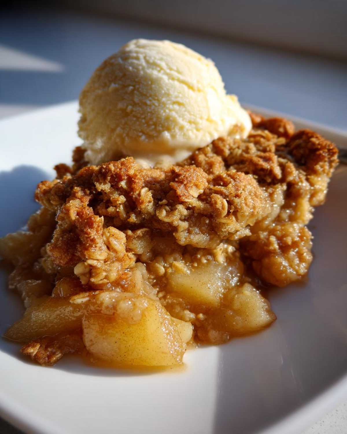 A close-up of a warm serving of pear crisp topped with a scoop of melting vanilla ice cream.