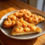 Three triangular pieces of golden brown shrimp toast topped with seasoned shrimp, served on a light gray plate.