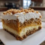 Close-up of a layered slice of pumpkin crunch dessert showing crust, cream cheese, pumpkin, and whipped topping.