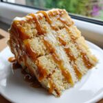 Close-up of a tall slice of caramel cake layered with cream filling and drizzled heavily with rich caramel sauce.