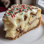 A thick slice of christmas tree cheesecake topped with white chocolate drizzle and festive red, green, and white sprinkles.