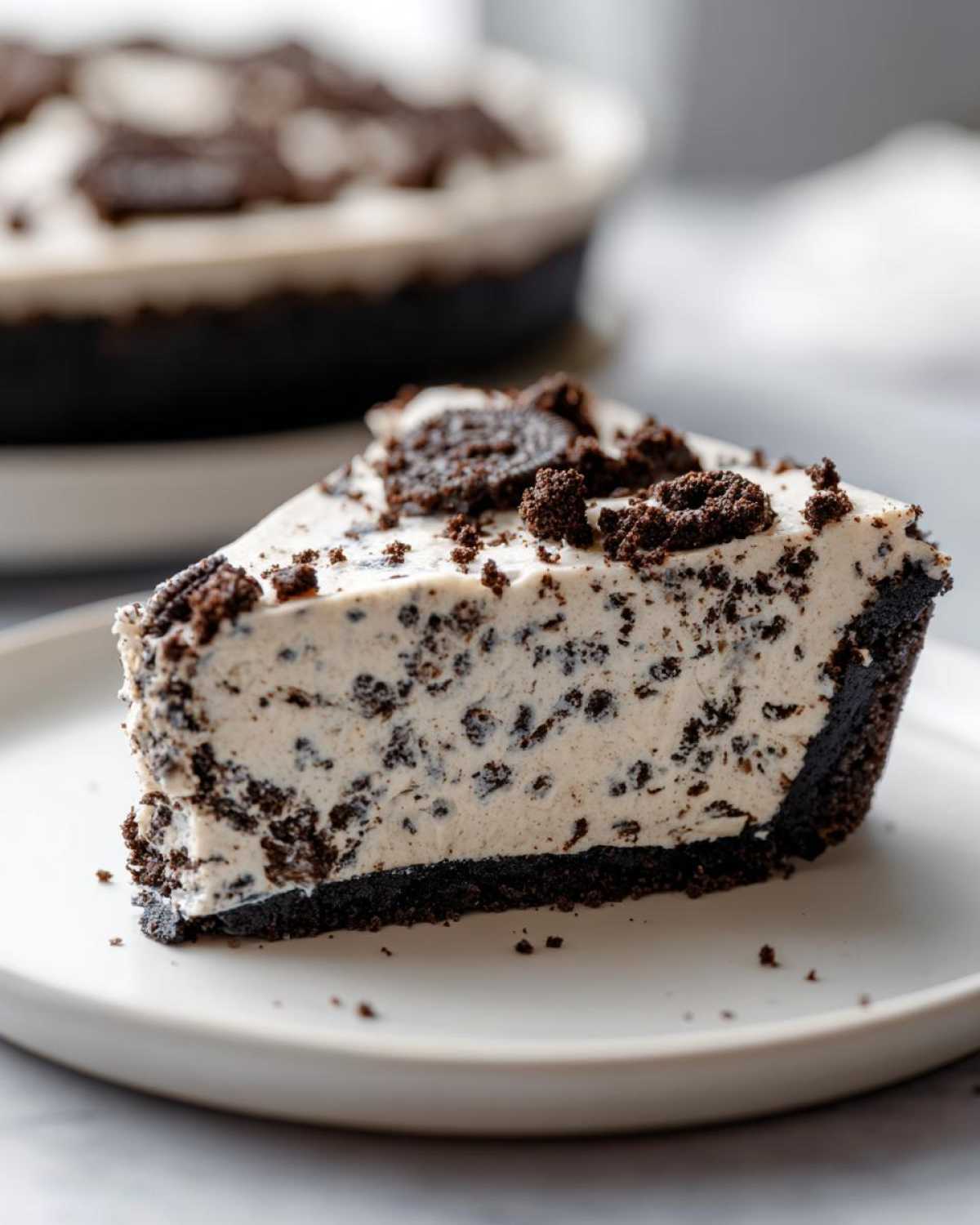 Close-up of a creamy slice of Oreo pie with a dark chocolate crust, topped with cookie pieces.