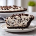 A close-up slice of creamy, no-bake Oreo pie with a dark chocolate crust and cookie crumbles on top.