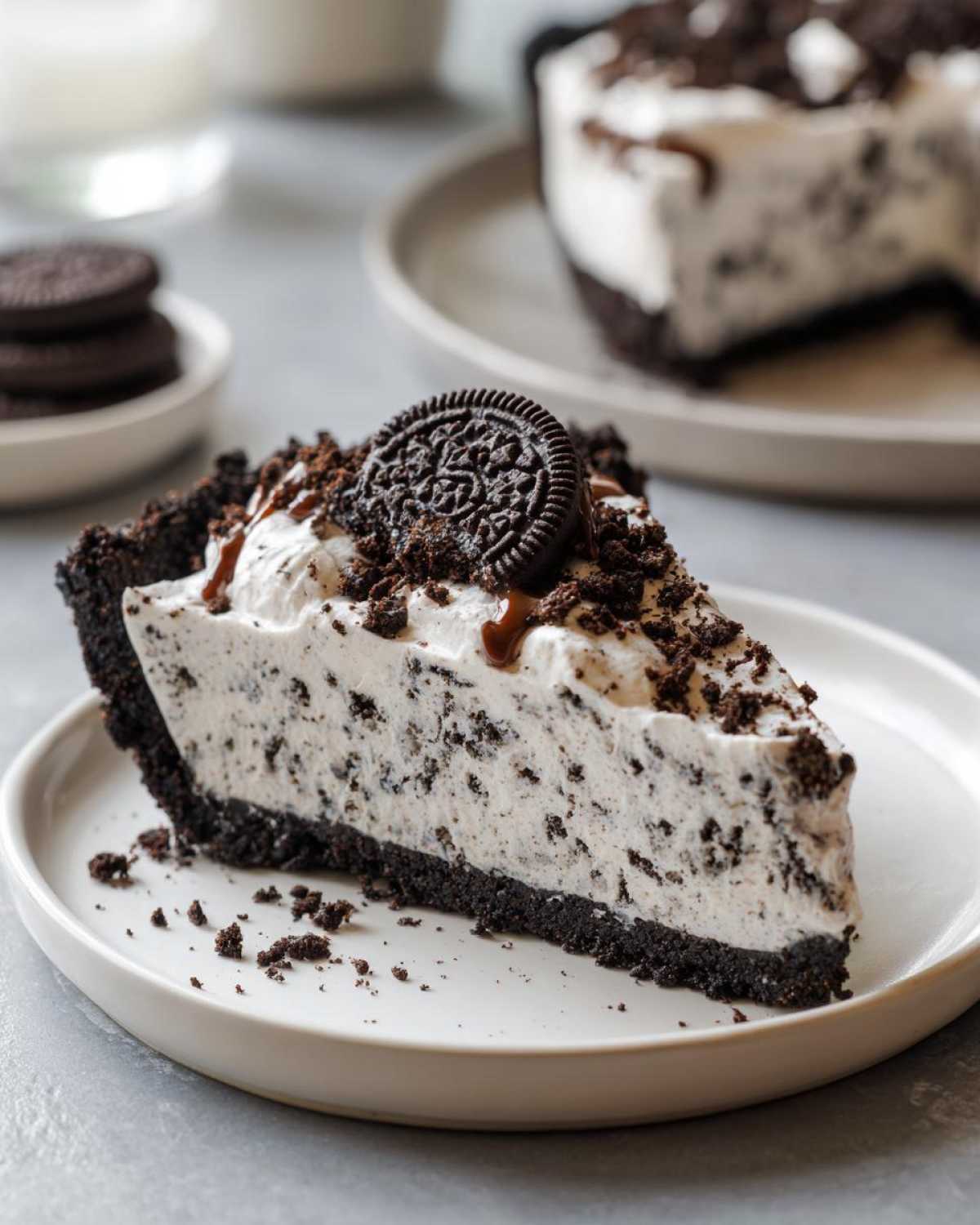 A generous slice of creamy, no-bake Oreo pie with a dark crust, topped with whipped cream, crumbs, and a whole cookie.