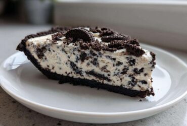 A generous slice of creamy, no-bake Oreo pie with a dark chocolate crust, served on a white plate.