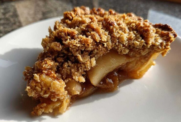 Close-up of a delicious slice of pear crisp showing baked, bubbly fruit filling and a thick, crunchy oat topping.