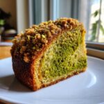 A close-up view of a moist slice of pistachio coffee cake featuring vibrant green swirls and a crunchy streusel topping.