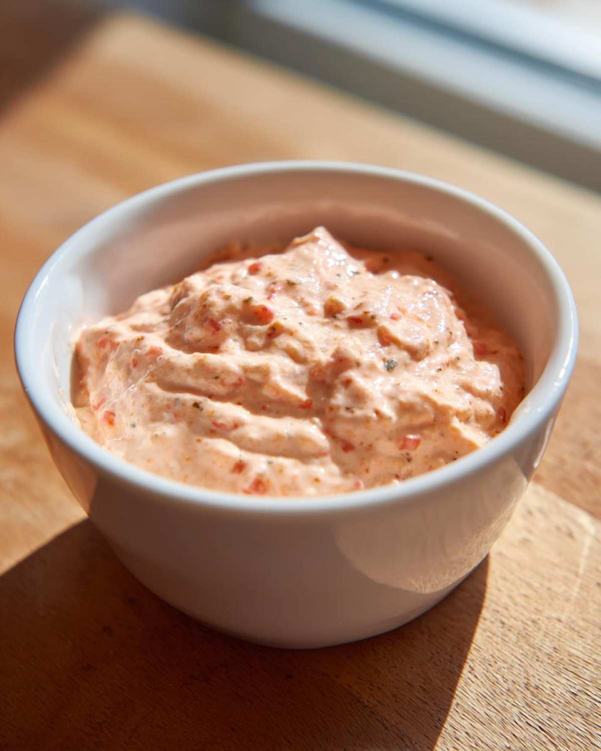 A close-up of creamy, pinkish smash burger sauce with visible red flecks in a small white bowl.