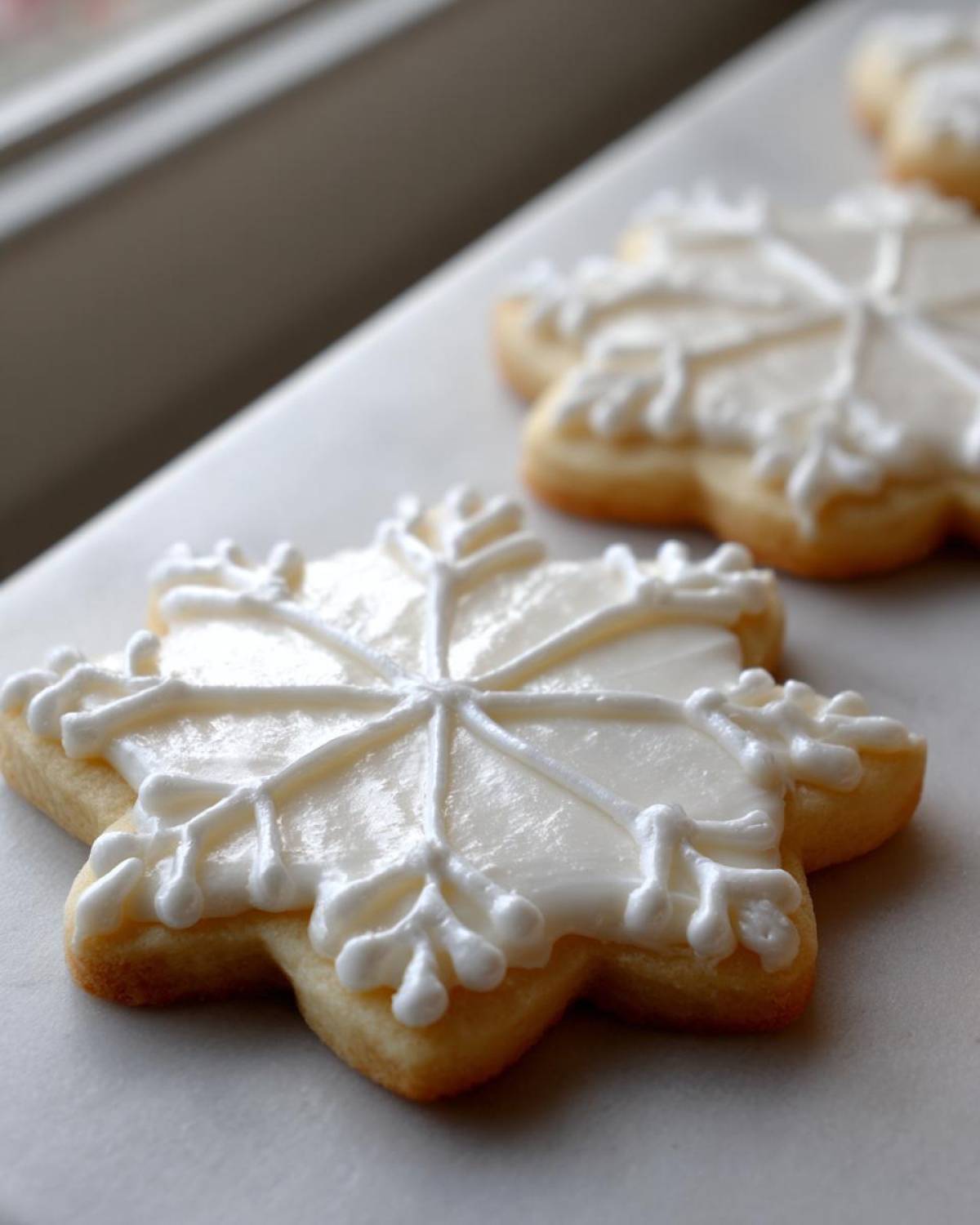 Close-up of a snowflake-shaped sugar cookie decorated with glossy white flood icing and piped royal icing details from the sugar cookie icing recipe.