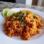 A plate of vibrant orange Spanish rice topped with fresh cilantro and two lime wedges on the side.