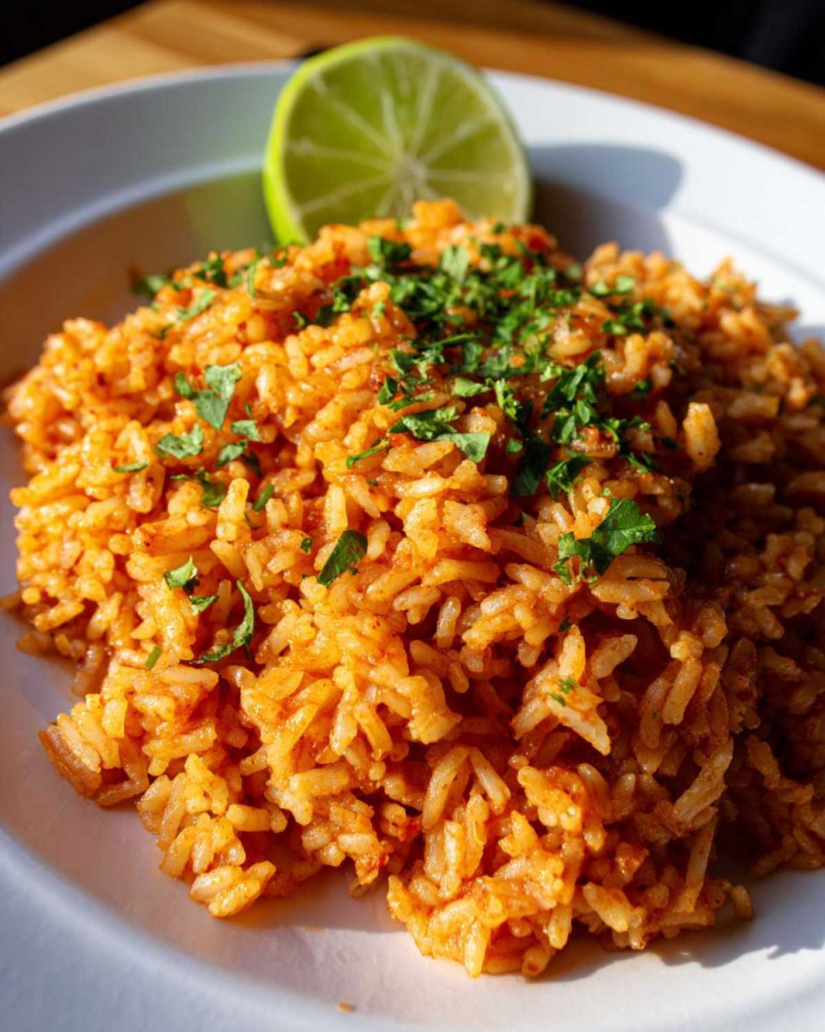 A close-up of vibrant orange Spanish rice garnished with fresh cilantro and a lime wedge.