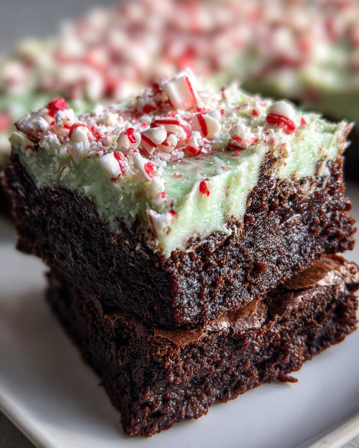 Two stacked, rich chocolate peppermint brownies topped with light green mint frosting and crushed candy canes.