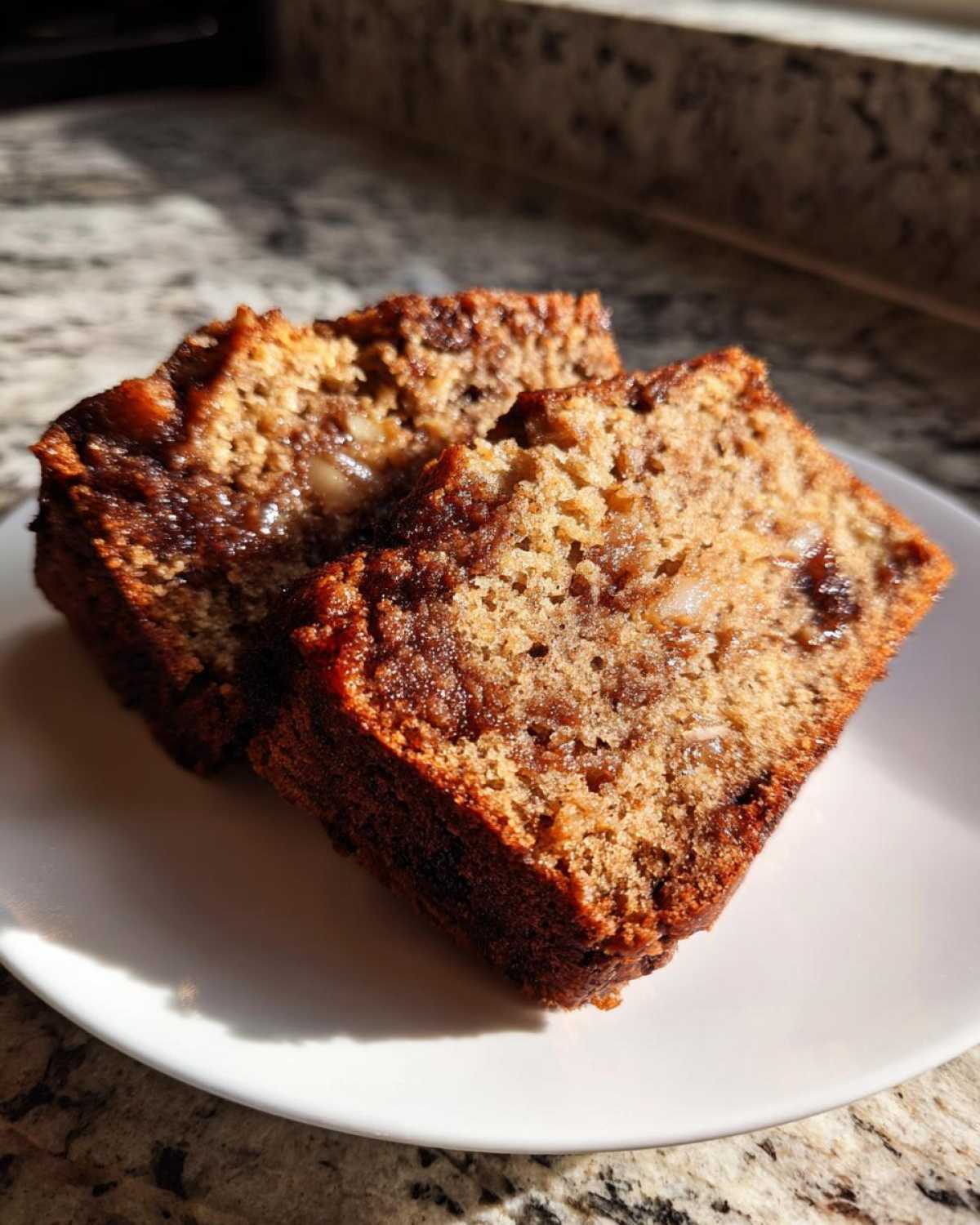 Two moist slices of apple bread showing visible chunks of apple and cinnamon swirl, served on a white plate.