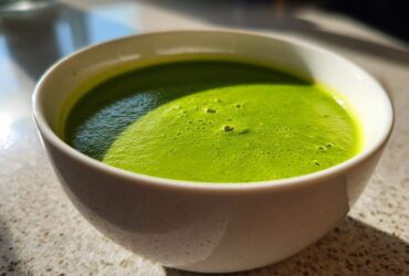Close-up of vibrant green asparagus soup with a slight froth, served in a white bowl.