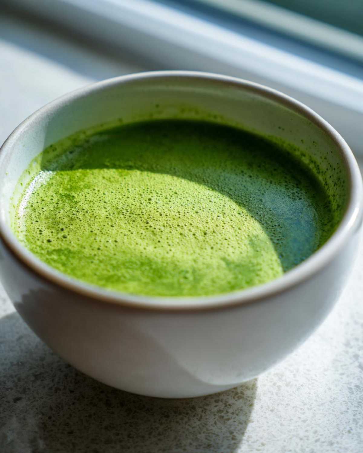 Close-up of vibrant green asparagus soup with a frothy top in a white bowl.