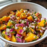 Close-up of vibrant homemade peach salsa featuring diced orange peaches, red onion, and cilantro in a white bowl.