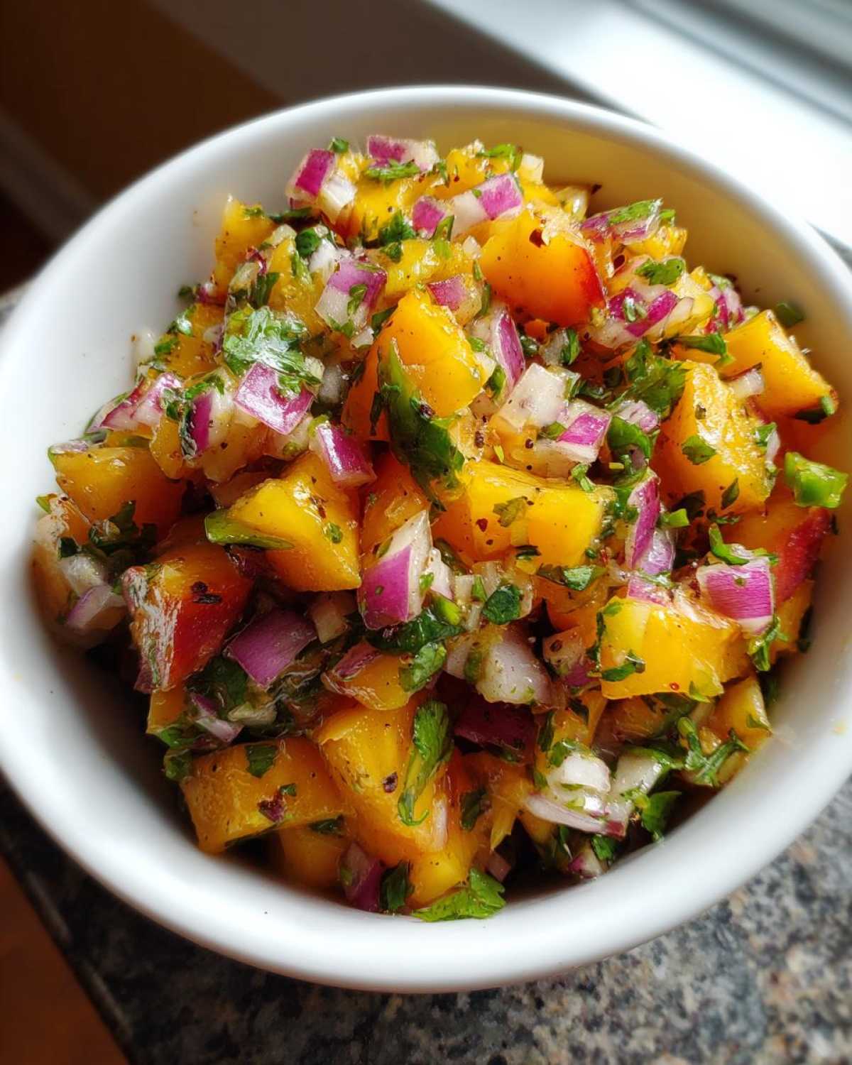 Close-up of fresh peach salsa featuring diced yellow peaches, red onion, and cilantro in a white bowl.