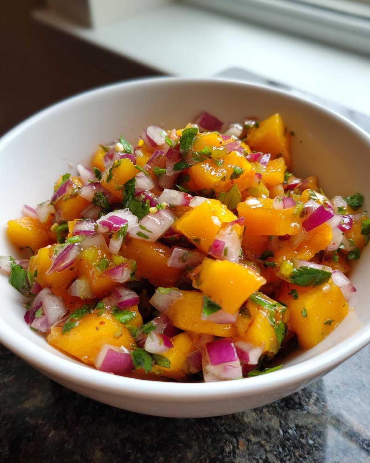 Close-up of fresh peach salsa featuring diced yellow peaches, red onion, and cilantro in a white bowl.