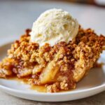 A close-up of a warm slice of pear crisp with a generous scoop of vanilla ice cream melting on top.
