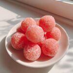 A close-up of several bright pink, round watermelon mochi balls dusted with white sugar on a small white plate.