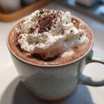 Close-up of a mug filled with rich whipped hot chocolate topped generously with whipped cream and chocolate shavings.