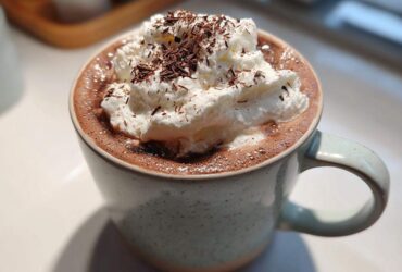 Close-up of a mug filled with rich whipped hot chocolate topped generously with whipped cream and chocolate shavings.