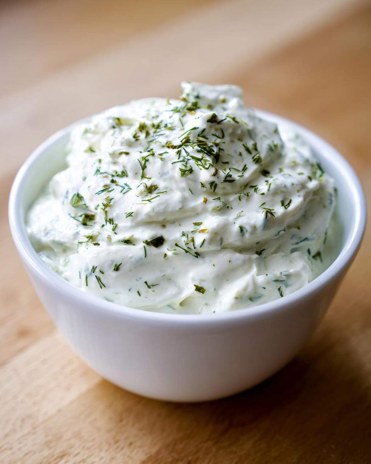 A close-up of thick, creamy 5-Minute Greek Yogurt Ranch Dip topped with fresh green herbs in a white bowl.