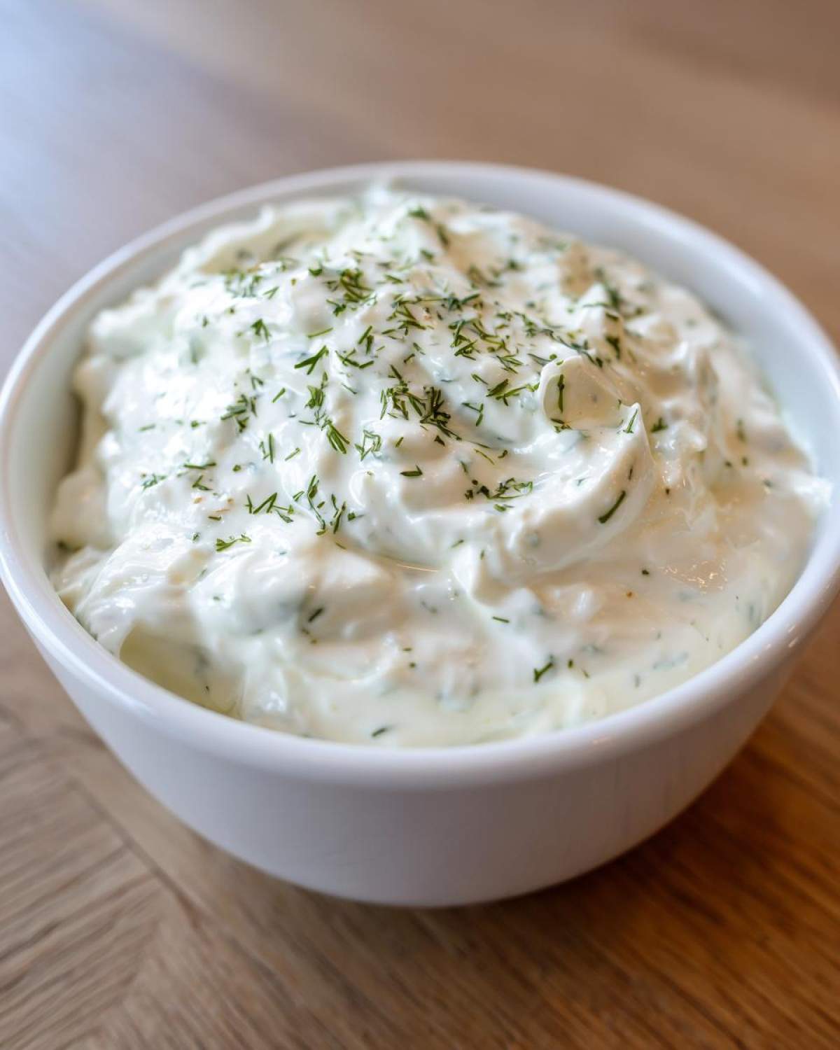 Close-up of thick, creamy 5-Minute Greek Yogurt Ranch Dip topped with fresh chopped dill in a white bowl.