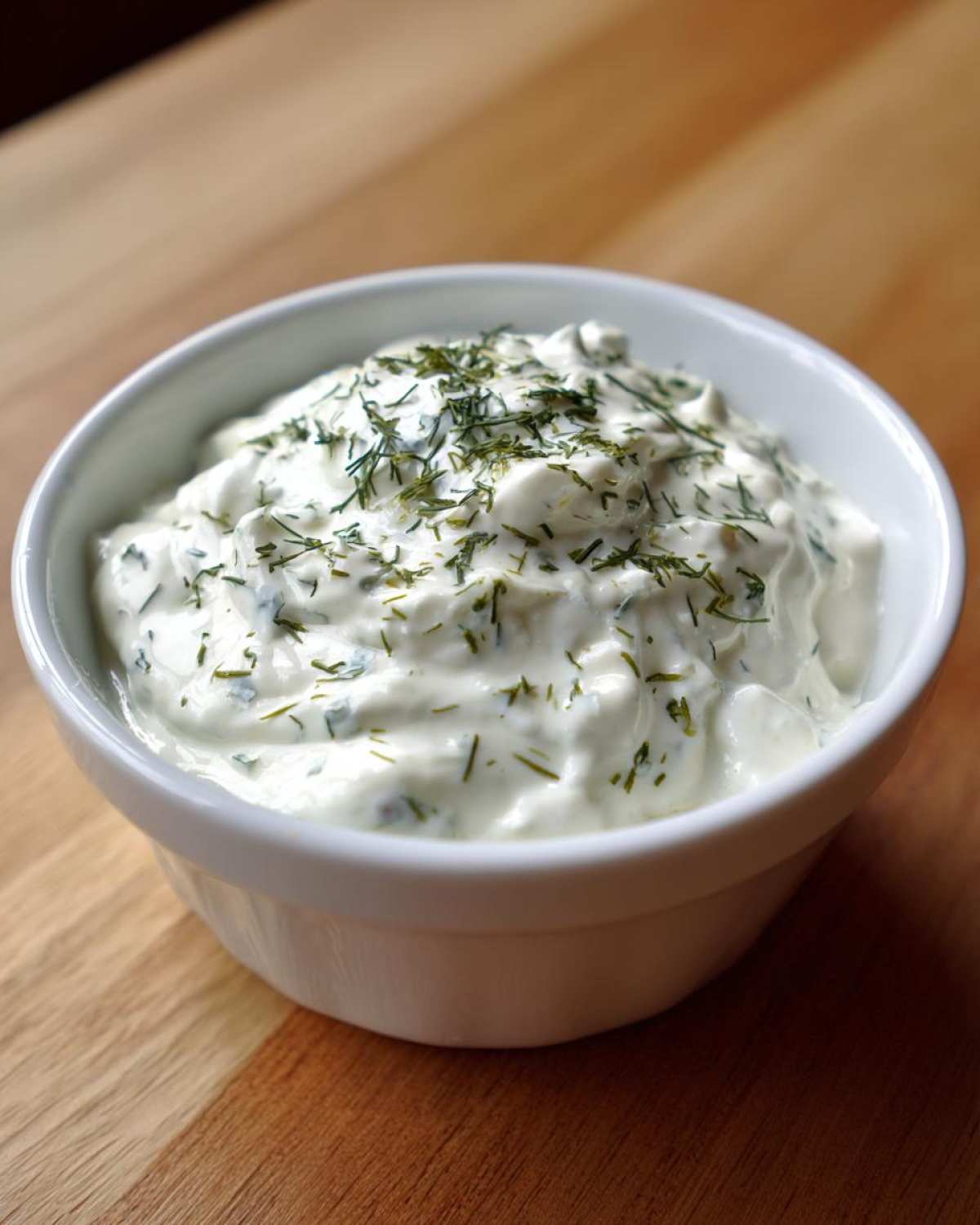 A small white bowl filled with creamy 5-Minute Greek Yogurt Ranch Dip, topped with fresh chopped dill.