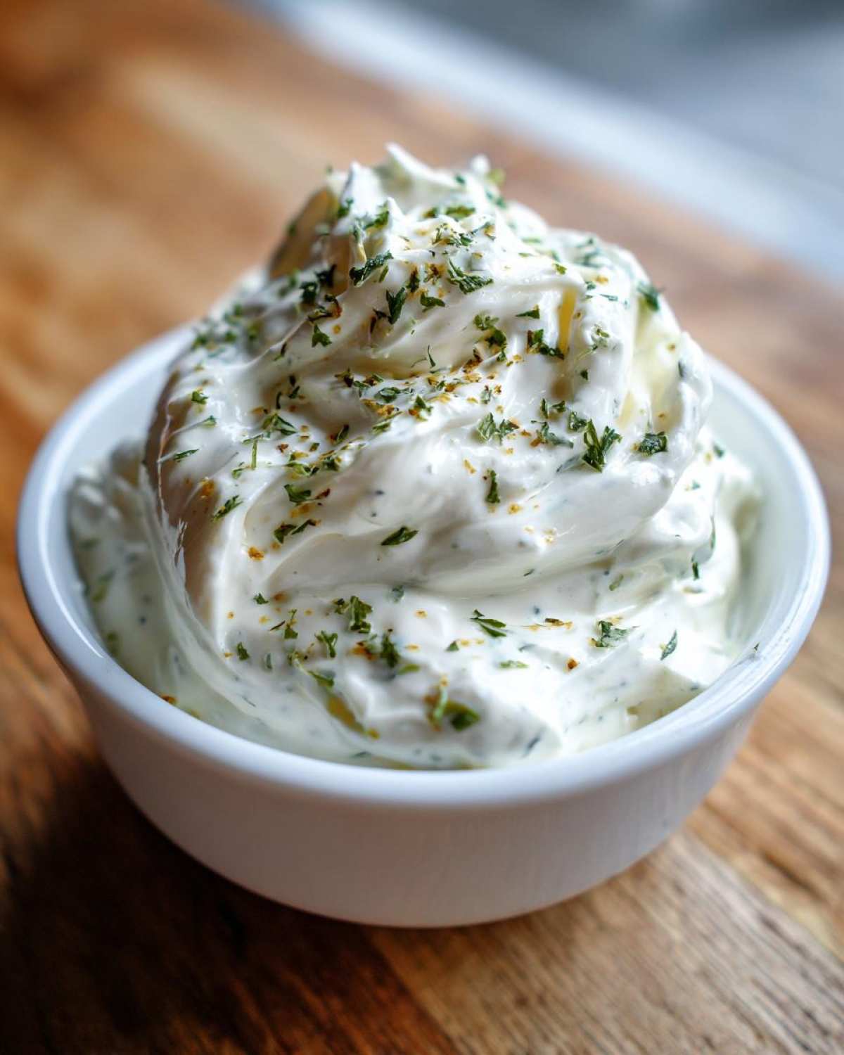 Close-up of creamy 5-Minute Greek Yogurt Ranch Dip swirled high in a white bowl, topped with dried herbs.