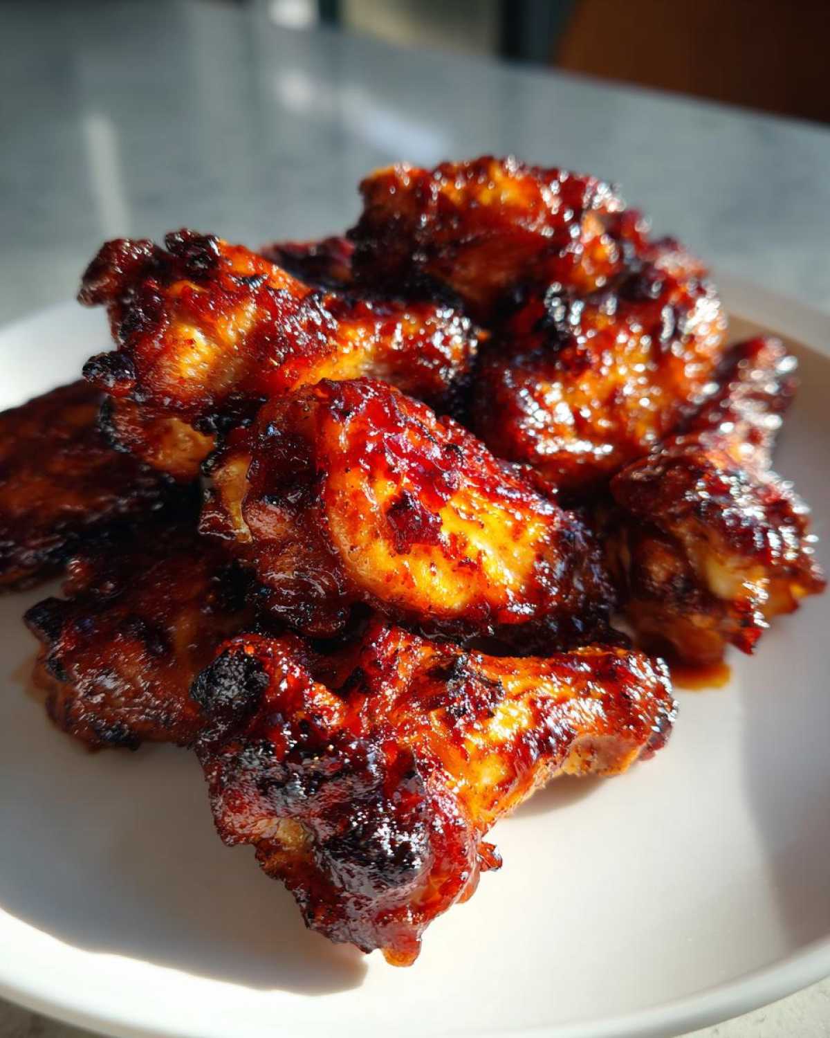 A pile of sticky, caramelized Air Fryer BBQ Chicken Wings glistening under bright light on a white plate.