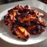 A pile of crispy, glossy Air Fryer BBQ Chicken Wings coated in dark, sticky sauce served on a white plate.