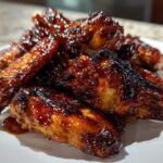 A close-up of a pile of sticky, caramelized Air Fryer BBQ Chicken Wings glistening with sauce on a white plate.