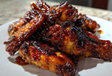 A close-up of a pile of sticky, caramelized Air Fryer BBQ Chicken Wings glistening with sauce on a white plate.