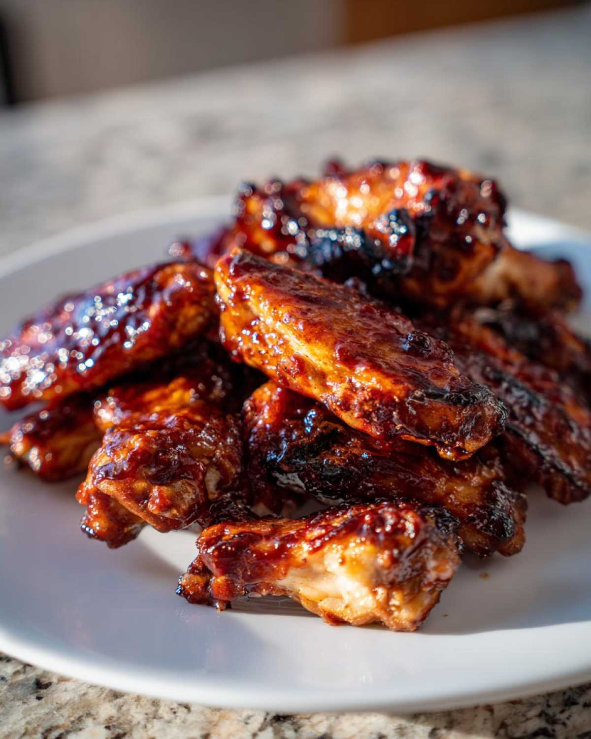 Close-up of sticky, caramelized Air Fryer BBQ Chicken Wings piled high on a white plate.