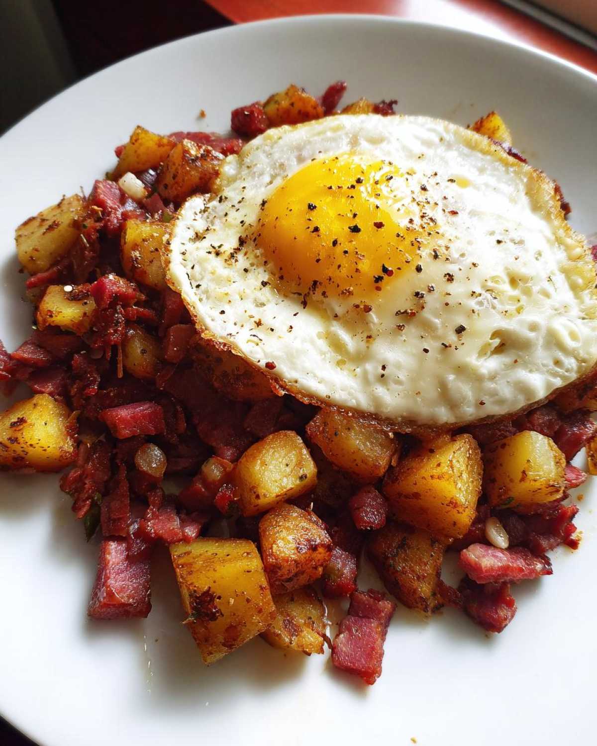 A plate of Air Fryer Corned Beef Hash with crispy potatoes, topped with a sunny-side-up egg seasoned with pepper.